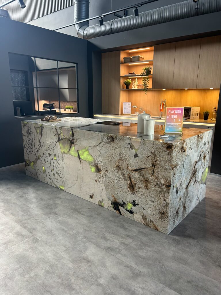 Moderne Küche mit Stein-Arbeitsplatte, gelben Akzenten und warm beleuchtetem Regal im Hintergrund.