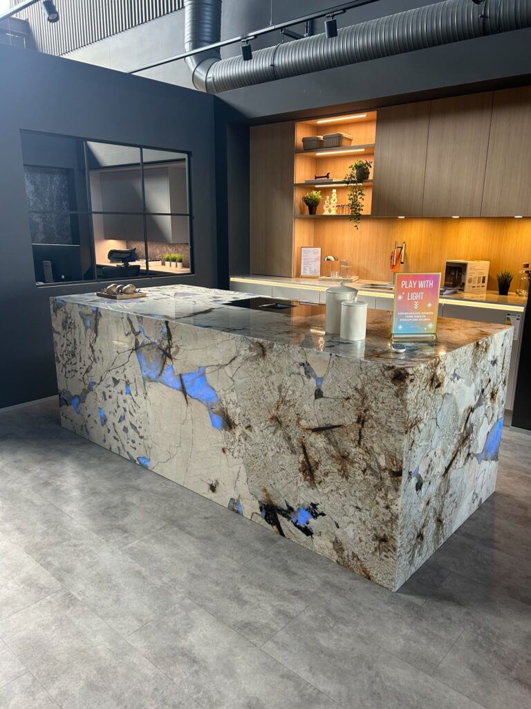 Moderne Küche mit großer Steininsel, warm beleuchteten Holzregalen und einem "PLAY WITH LIGHT"-Schild.