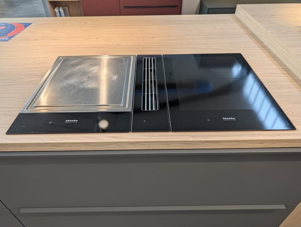 Moderne Küche mit Miele Induktionskochfeldern, Holzarbeitsplatte und integriertem Lüftungssystem.