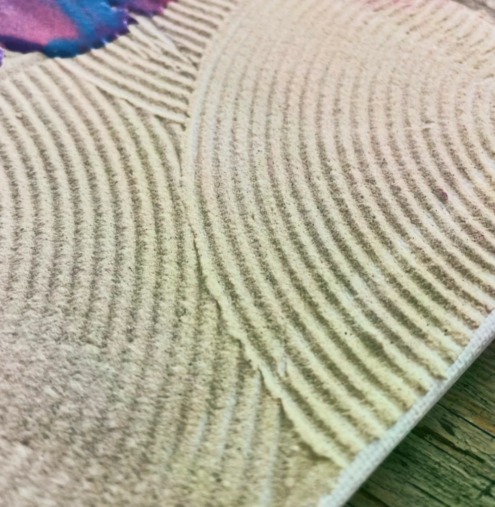 Nahaufnahme eines Zen-Sandmusters mit konzentrischen Linien und blauen sowie lila Farbklecksen.