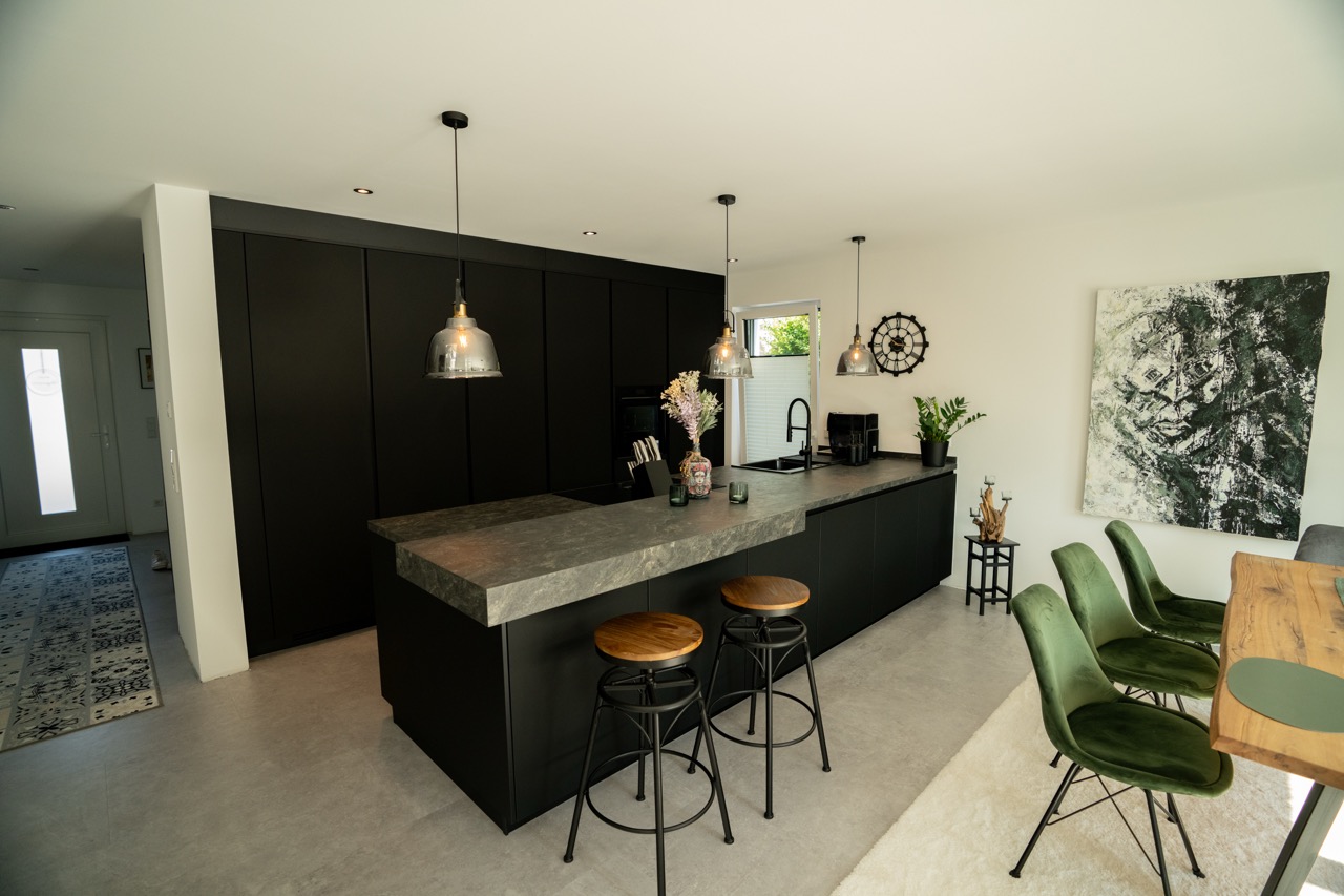 Moderne Küche mit schwarzer Kücheninsel, Holzsitzhockern, grünen Samtstühlen und abstraktem Kunstwerk.