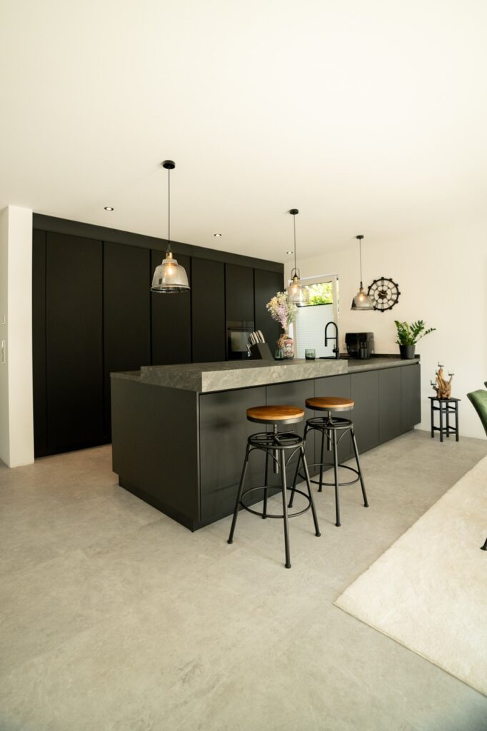 Moderne Küche mit grauer Steininsel, schwarzen Schränken, Holzbarhockern und stilvoller Beleuchtung.