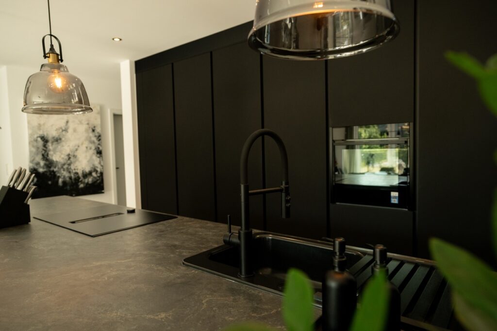 Moderne, minimalistische Küche mit dunklen Schränken, Stein-Arbeitsplatte und stilvollen Hängeleuchten.