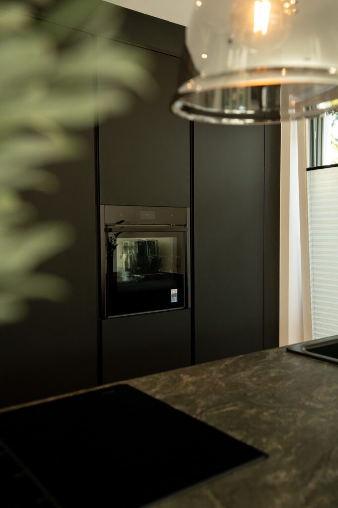Moderne Küche mit dunklem Design, eingebautem Backofen, marmorierter Arbeitsplatte und Hängelampe.