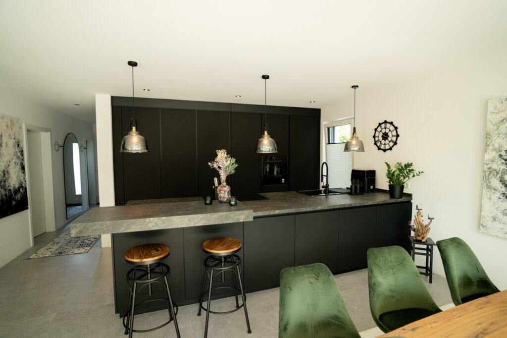 Moderne Küche mit grauer Insel, Holz-Metall-Hockern, industriellen Lampen und grünen Stühlen.