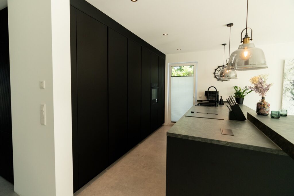 Moderne, minimalistische Küche mit dunkler Arbeitsplatte, schwarzen Schränken und grünen Pflanzen.