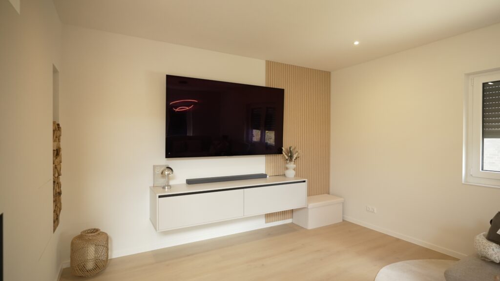 Modernes Wohnzimmer mit Flachbildfernseher, weißem Sideboard, Holzverkleidung und natürlichem Dekor.