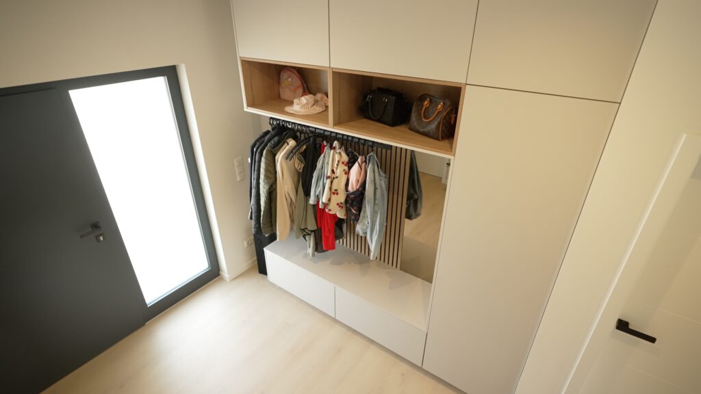 Moderner Flur mit hellem Kleiderschrank, bunten Jacken, Taschen und Accessoires; warme, einladende Atmosphäre.