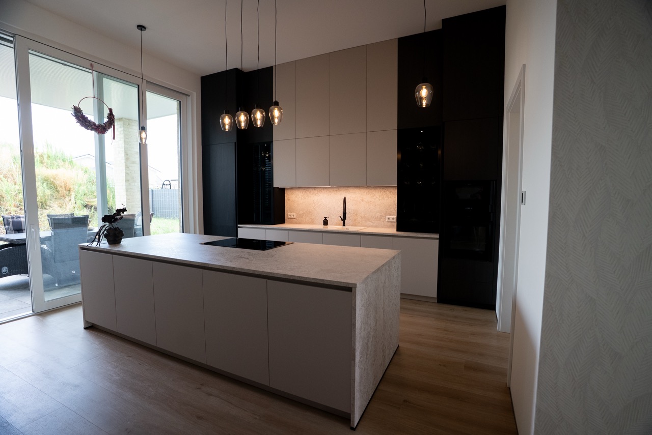 Moderne, minimalistische Küche mit heller Insel, schwarzen Schränken und warmem Licht.