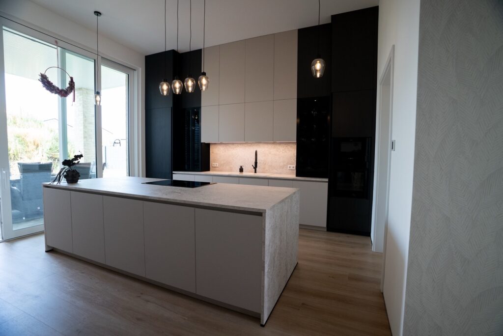 Moderne, minimalistische Küche mit heller Insel, dunklen Schränken und großer Glasfront für viel Licht.