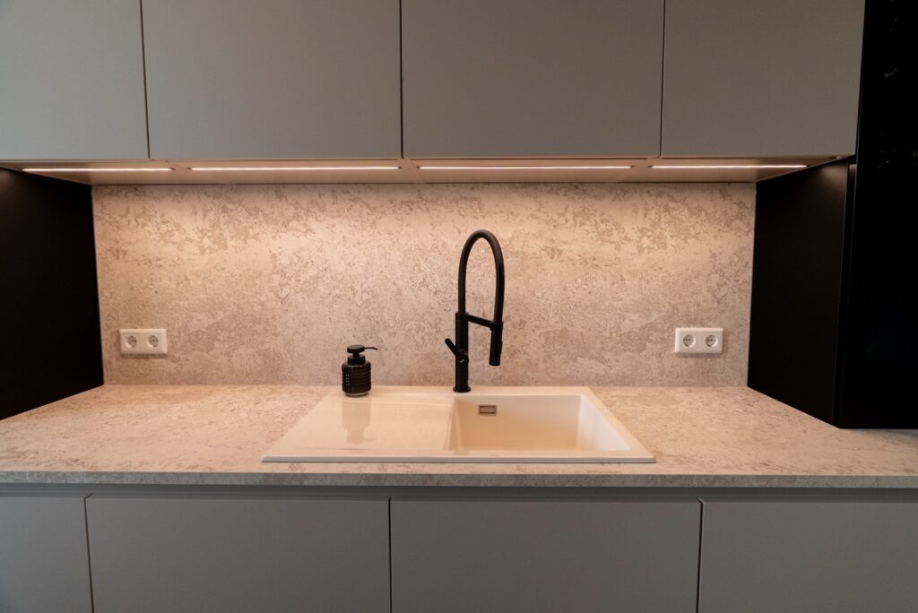 Moderne Küche mit beiger Arbeitsplatte, schwarzem Wasserhahn und grauen Schränken, minimalistisch gestaltet.