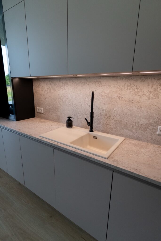 Moderne Küche mit heller Arbeitsplatte, schwarzem Wasserhahn und grauen Oberschränken, minimalistisch gestaltet.