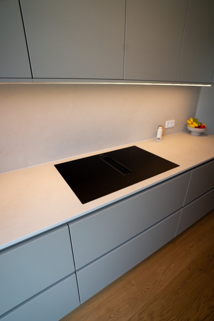 Moderne, minimalistische Küche mit grauen Schränken, hellem Induktionskochfeld und Obstschale.