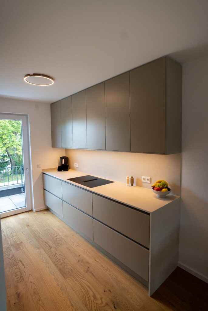 Moderne, minimalistische Küche mit grauen Schränken, hellem Holzfußboden und bunter Obstschale.