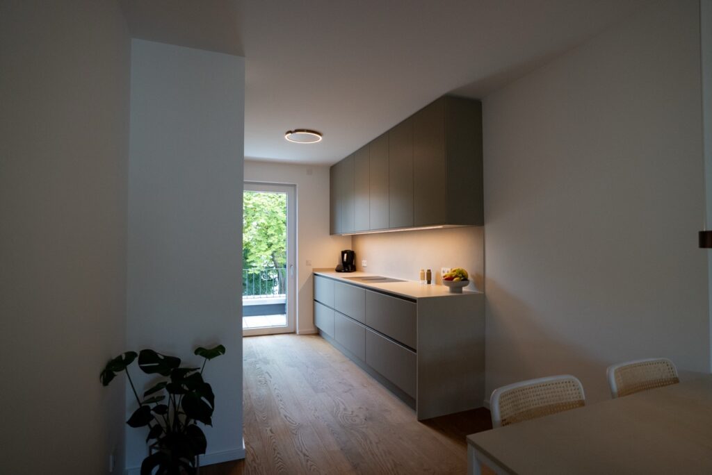 Moderne, minimalistische Küche mit grauen Schränken, Holzboden, Esstisch und viel natürlichem Licht.