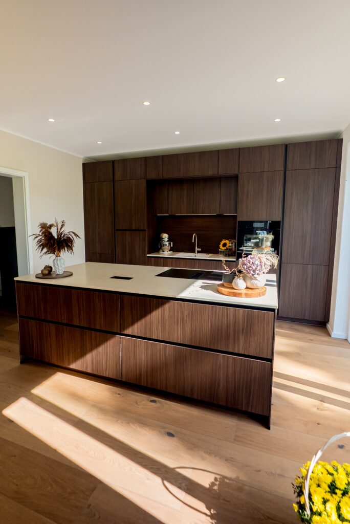 Moderne Küche mit dunklen Holzschränken, heller Arbeitsplatte, Kücheninsel und dekorativen Elementen.