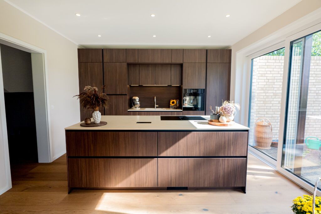 Moderne, aufgeräumte Küche mit heller Insel, dunklen Holzfronten und dekorativen Pflanzen.