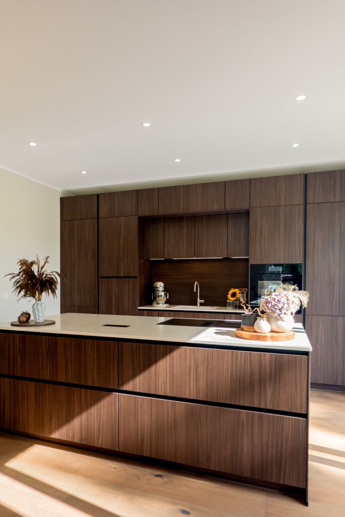 Moderne Küche mit dunklen Holzschränken, heller Insel, Blumenarrangements und sanfter Beleuchtung.