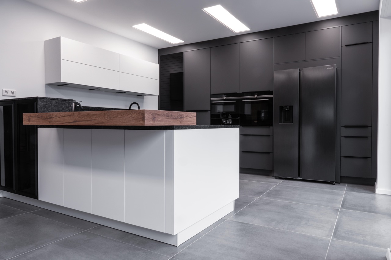 Moderne, minimalistische Küche mit weißer Insel, schwarzen Schränken und Holzdetails. Keine Personen sichtbar.