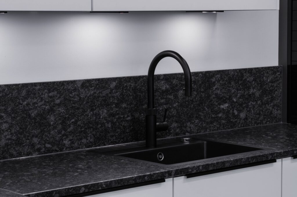 Moderne Küche mit schwarzer Armatur, dunkler Spüle und Granit-Arbeitsplatte vor weißem Hintergrund.