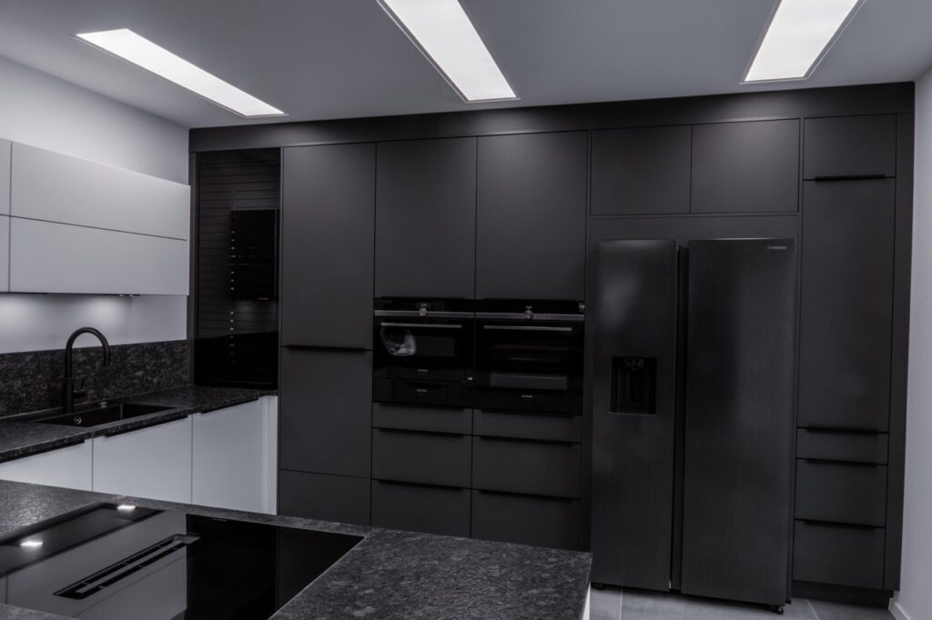 Moderne Küche in dunklem Grau mit Einbaugeräten, Kochfeld, Waschbecken und eleganter Beleuchtung.