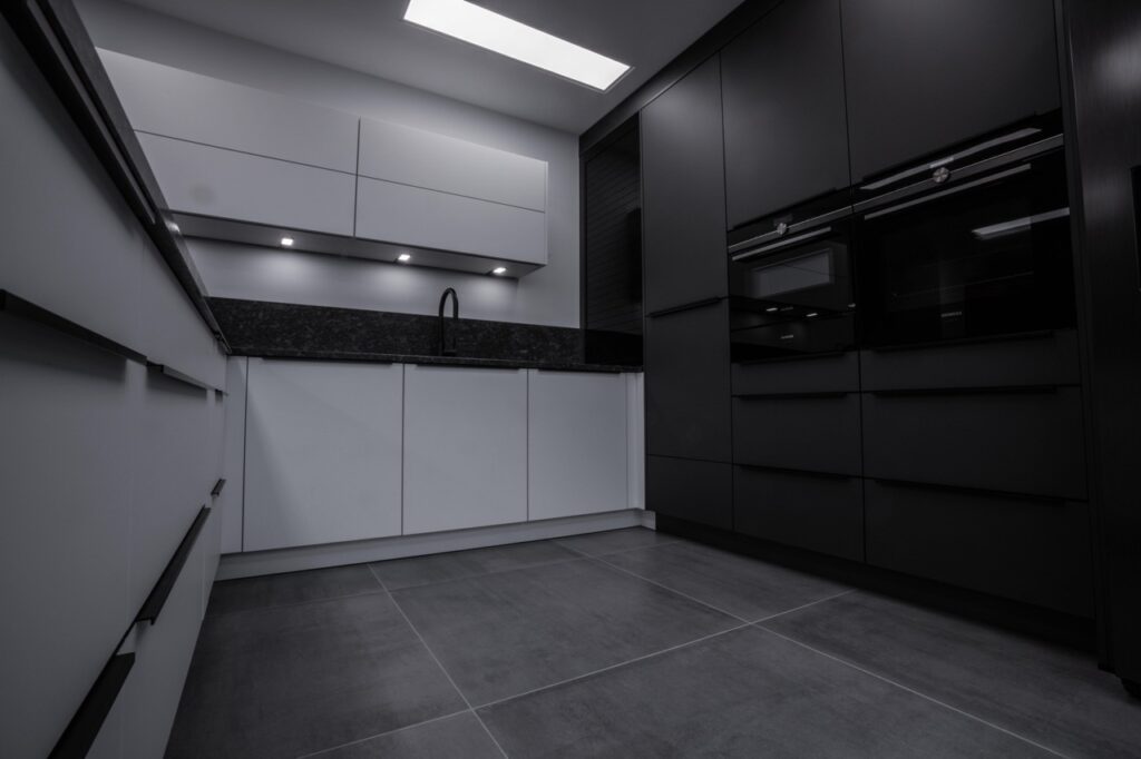 Moderne, minimalistische Küche mit weißen und schwarzen Schränken, dunkler Arbeitsplatte und eingebauten Geräten.
