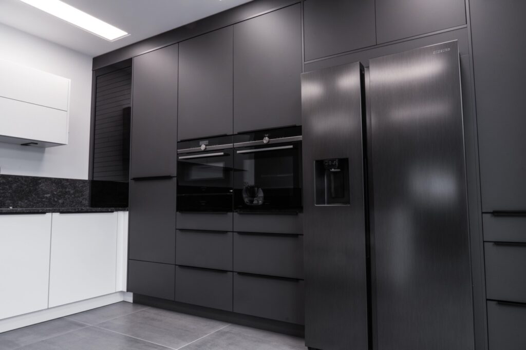 Moderne, minimalistische Küche mit Edelstahlkühlschrank, dunklen Schränken und heller Arbeitsplatte.