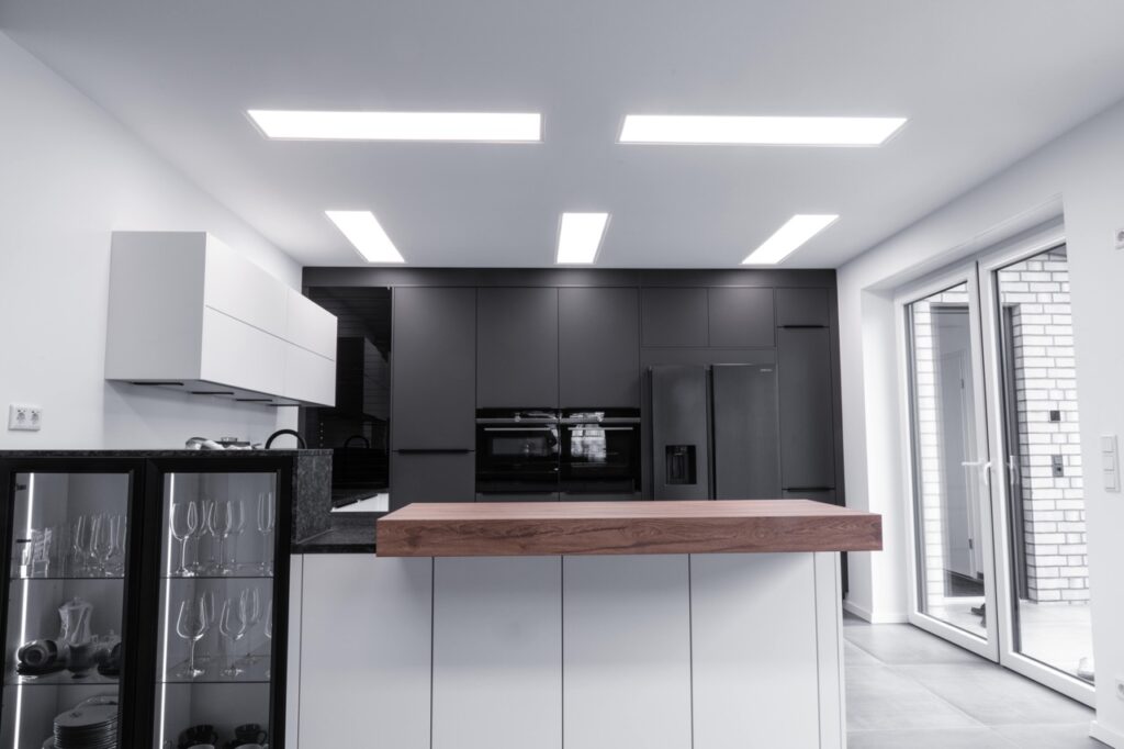 Moderne Küche mit Holzarbeitsplatte, Edelstahlkühlschrank, weißen und schwarzen Schränken, viel Licht.