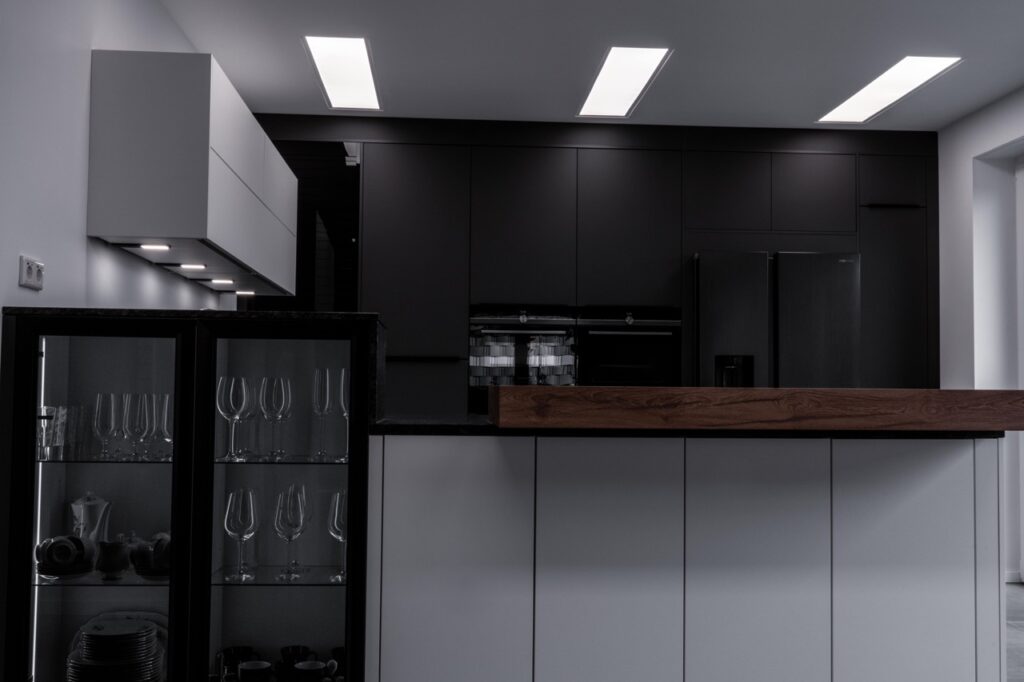 Moderne, minimalistische Küche mit dunklen Tönen, Holzarbeitsplatte und Glasvitrine. Keine Personen sichtbar.