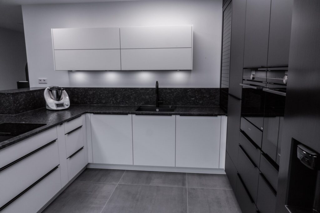 Moderne, minimalistische Küche in Schwarz-Weiß mit Einbaugeräten und einem Küchenhelfer auf der Arbeitsplatte.