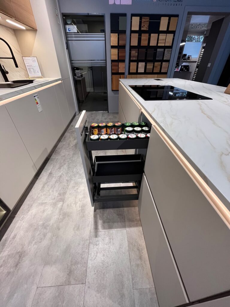 Moderne Küche mit grauen Schränken, offenem Auszug mit Dosen und Materialproben an der Wand.
