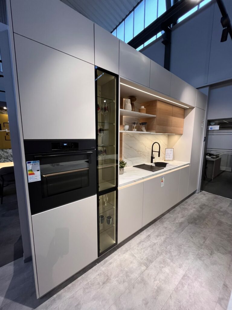 Moderne Küche mit hellen Schränken, schwarzem Backofen, Marmorarbeitsplatte und offenen Holzregalen.