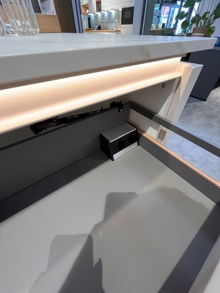 Moderne Küche mit geöffneter Schublade, die eine Steckdose zeigt; stilvolles, funktionales Design.