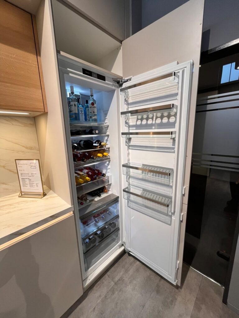 Ein offener Kühlschrank in einer modernen Küche zeigt ordentlich angeordnete Getränkeflaschen.