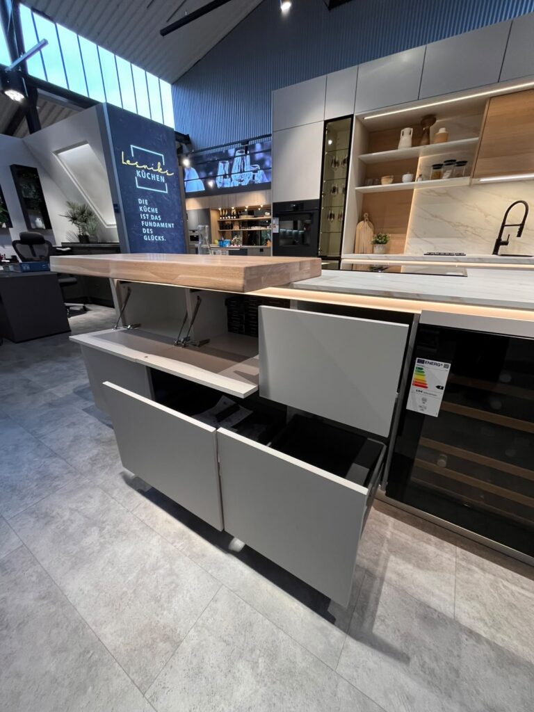 Moderne Küchenausstellung mit offenen Schränken, Holzarbeitsplatte, Backofen und Weinkühlschrank.