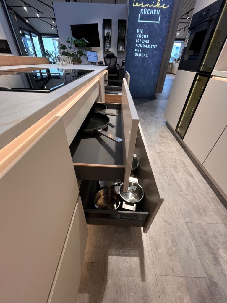 Moderne Küchenausstellung mit offener Schublade, Pfannen, Töpfen und eleganter Kücheninsel.