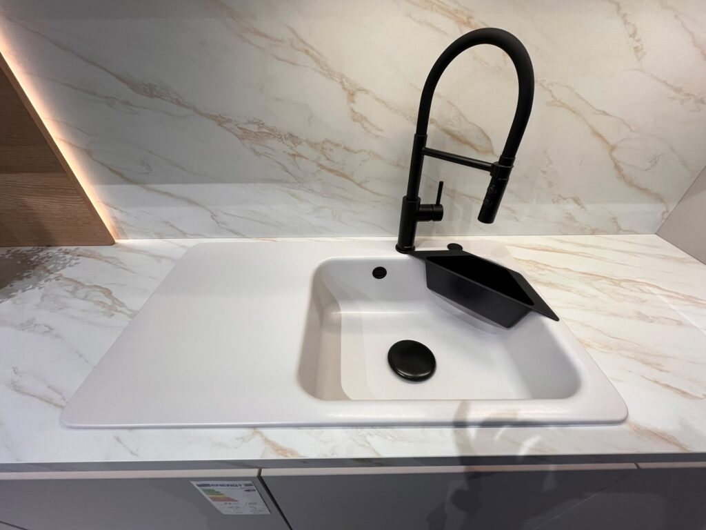 Moderne weiße Küchenspüle mit schwarzem Wasserhahn und Abtropfgestell auf Marmorarbeitsplatte.