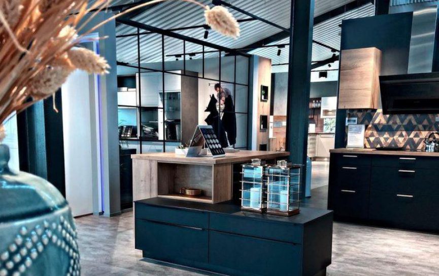 Moderne Küchenausstellung mit zentralem Tresen, Schränken, blauer Vase und einer Person im Hintergrund.