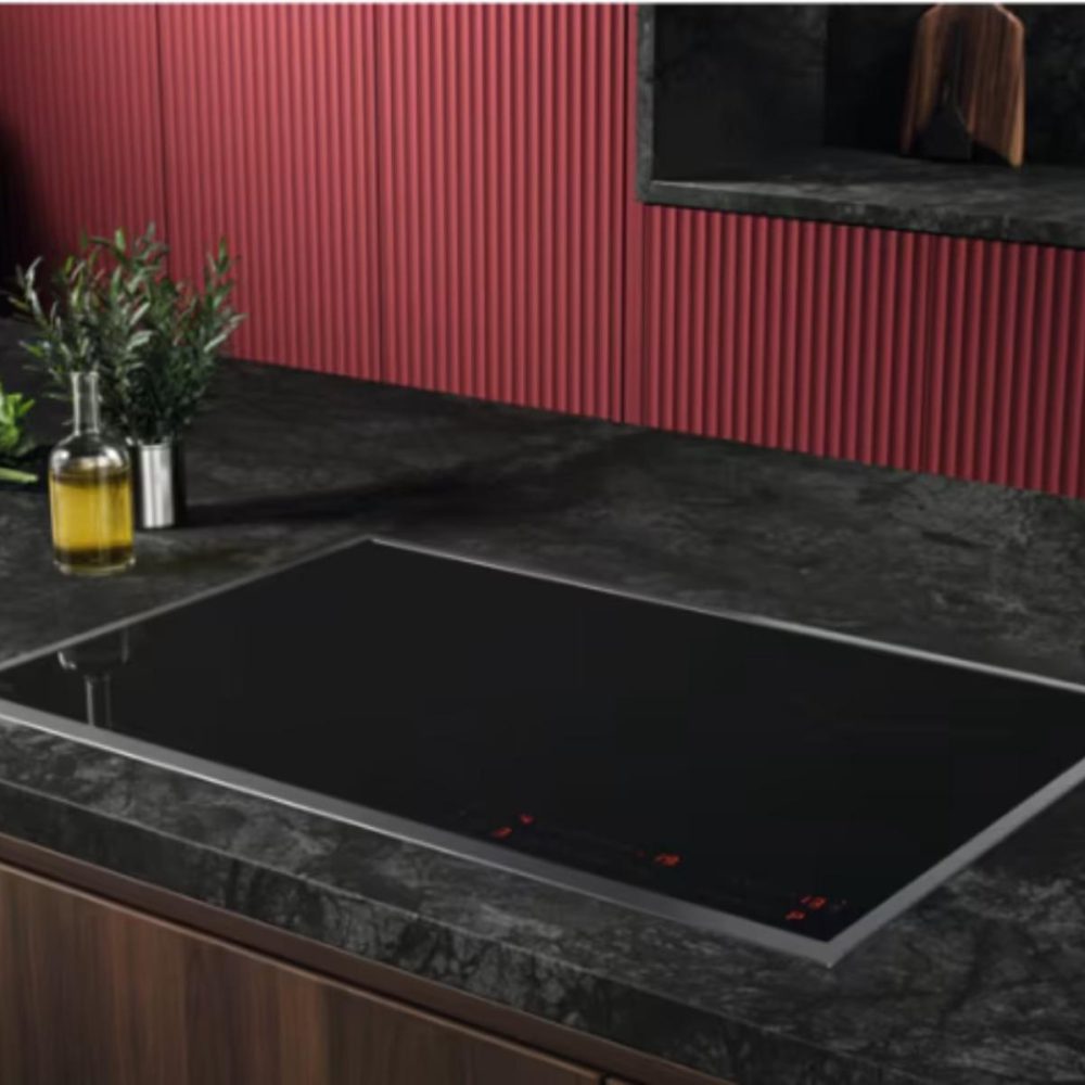 Moderne Küche mit schwarzem Induktionskochfeld, Ölflasche, Kräutern und grünem Salat auf dunkler Arbeitsplatte.