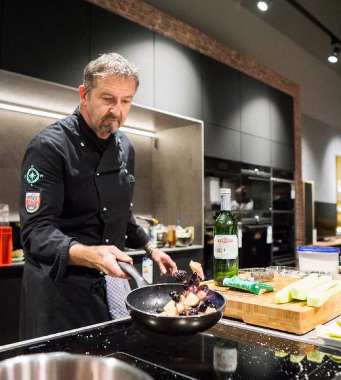 Ein Koch in schwarzer Uniform brät Gemüse in einer modernen Küche mit Zutaten auf der Insel an.