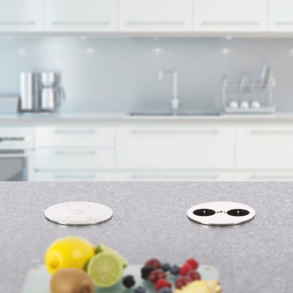 Moderne Küche mit grauer Arbeitsplatte, integriertem Steckdosen und buntem Obst auf einem Schneidebrett.