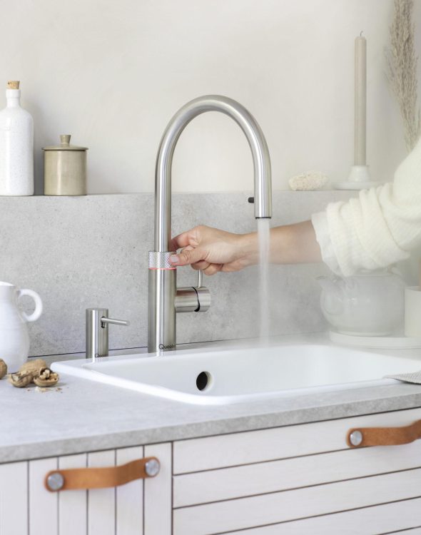 Ein moderner Edelstahl-Wasserhahn in einer minimalistischen Küche, aus dem heißer Dampf aufsteigt.