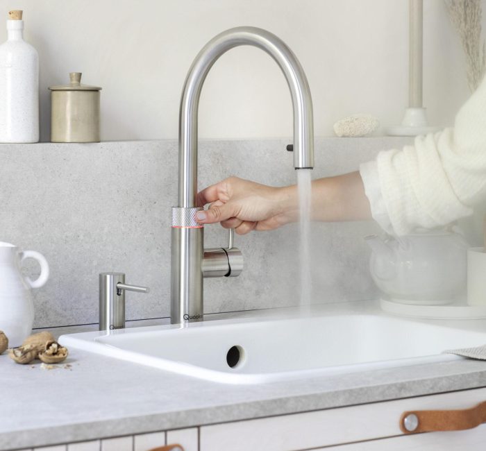 Ein moderner Edelstahl-Wasserhahn in einer minimalistischen Küche, aus dem heißer Dampf aufsteigt.