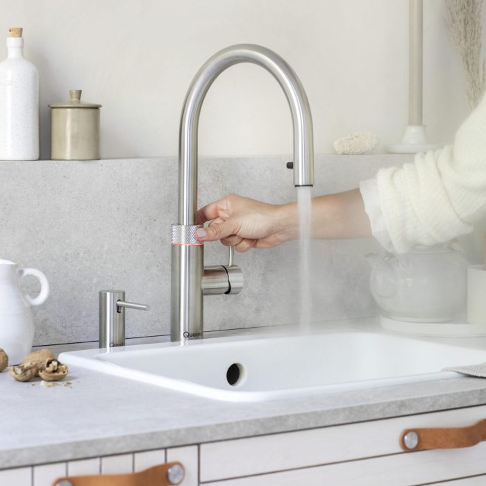 Ein moderner Edelstahl-Wasserhahn in einer minimalistischen Küche, aus dem heißer Dampf aufsteigt.