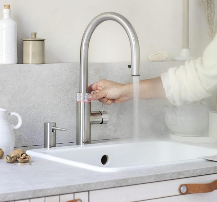 Ein moderner Edelstahl-Wasserhahn in einer minimalistischen Küche, aus dem heißer Dampf aufsteigt.