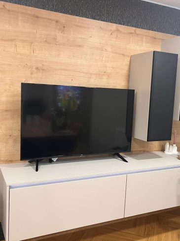 Modernes Wohnzimmer mit Flachbildfernseher, schwebendem Sideboard, Pflanzen und Holzverkleidung.