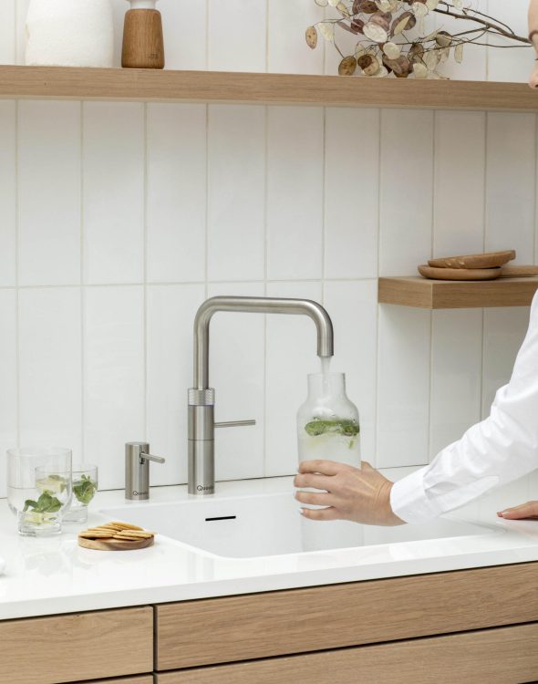 Fusion Square_Voll-Edelstahl Moderne Küche mit Edelstahl-Wasserhahn, Hand füllt Glaskaraffe, Gläser mit Minze, minimalistische Deko.