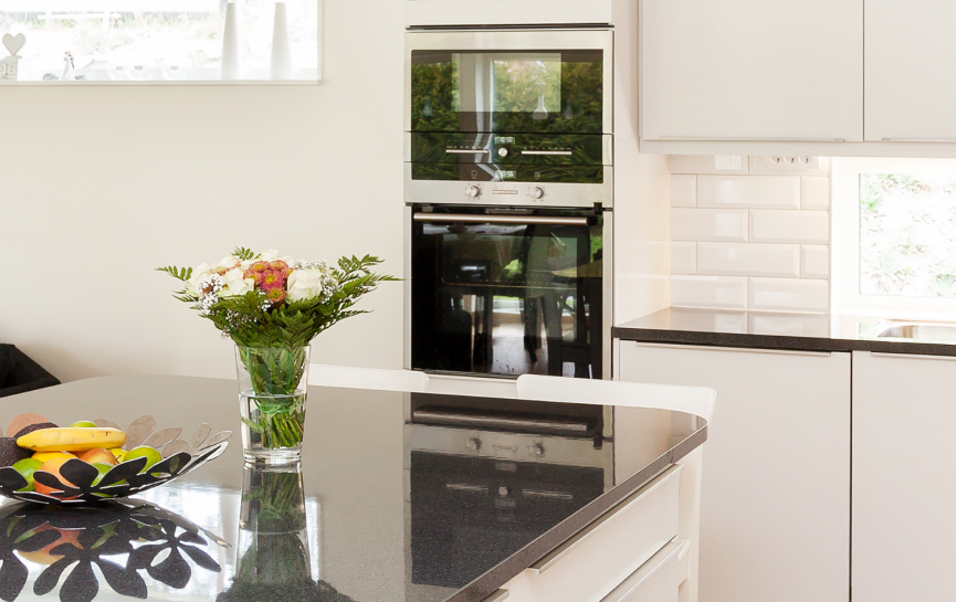 Moderne, helle Küche mit weißem Design, dunkler Arbeitsplatte, Blumen, Früchten und Holzboden.