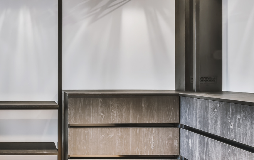 Moderner, leerer Kleiderschrank mit schwarzen Kleiderbügeln, dunklen Holzregalen und beigem Hocker.