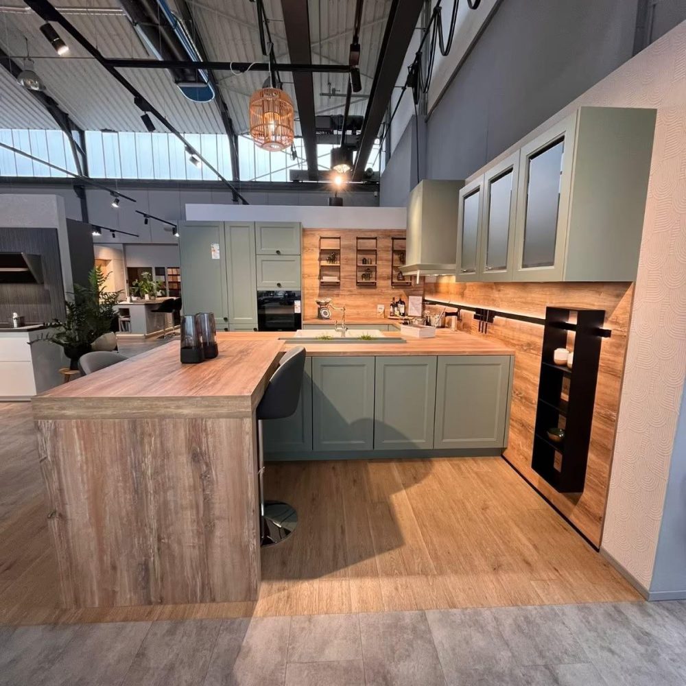 Moderne Ausstellungsküche mit grünen Schränken, Holzarbeitsplatte und Barhockern in gemütlicher Atmosphäre.